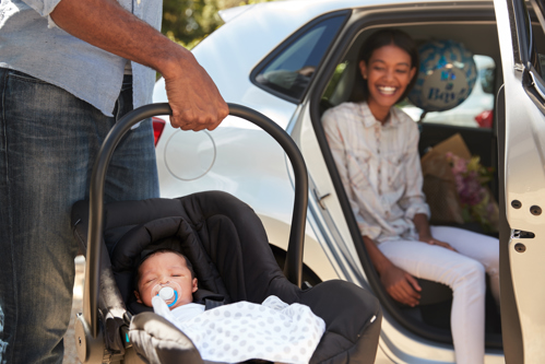 Young girl in a car smiling at baby being carried in a car seat